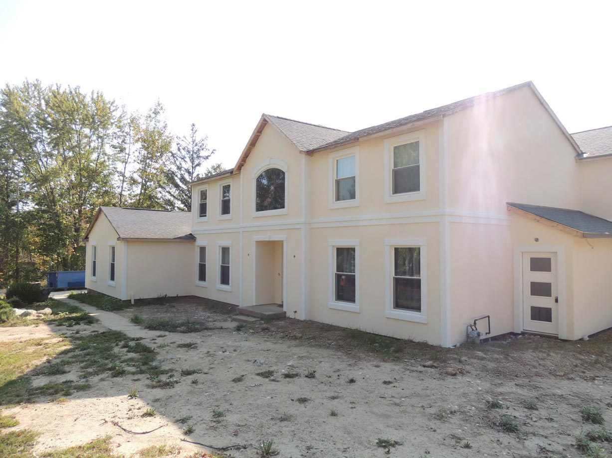 An apartment building exterior in pre-renovation condition with bare ground and weathered siding.