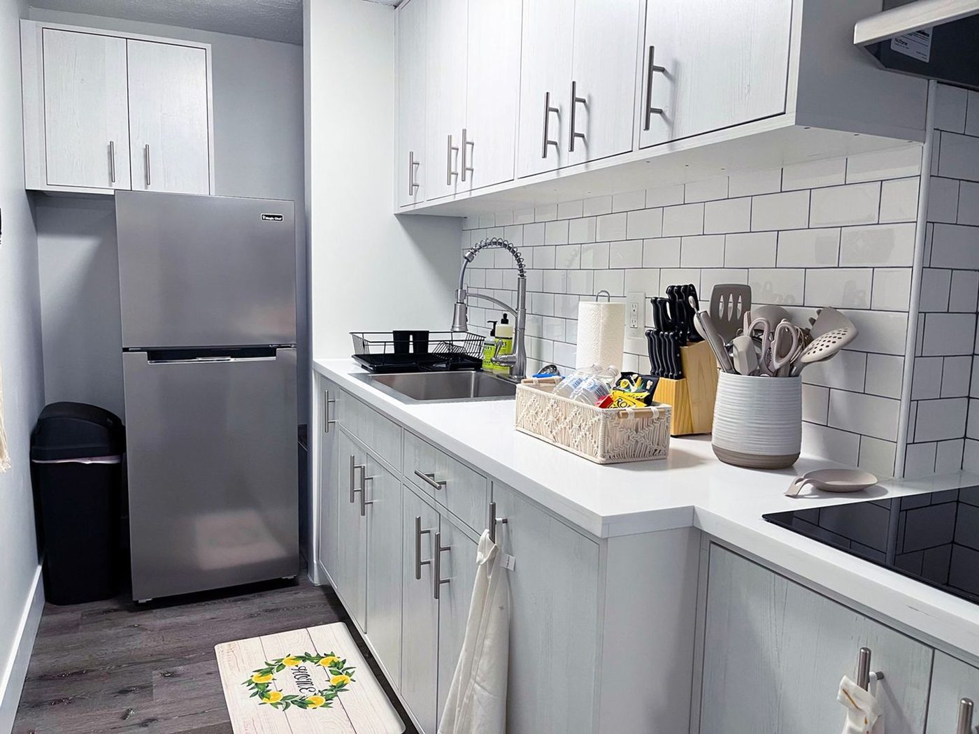 The same kitchen type after renovation, with white shaker cabinets, subway tile, stainless appliances and luxury vinyl plank flooring.
